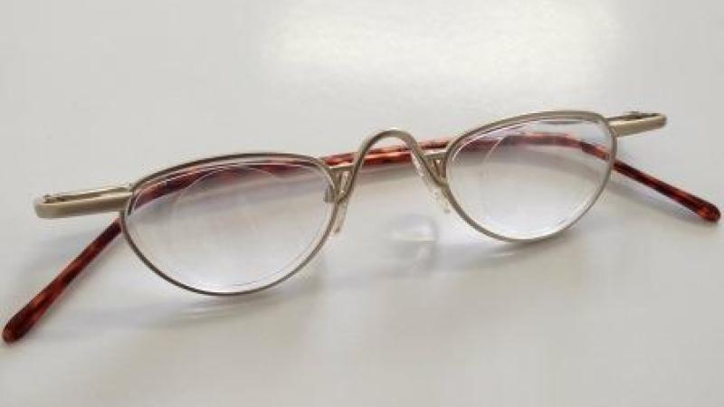 Auf einem hellen Untergrund liegt eine Halbbrille mit eingeklappten Bügeln. - Ausführliche Bildbeschreibung verfügbar unter: https://www.amd-netz.de/bildbeschreibung.php?b=49