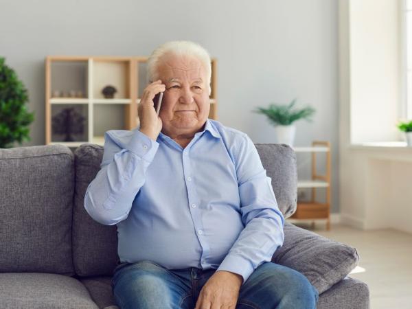 Ein älterer Mann sitzt auf einem Sofa und hält ein Handy ans Ohr.