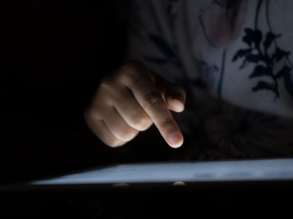 Vor einem dunklen Hintergrund ist eine Hand über einem beleuchteten Tablet zu sehen.